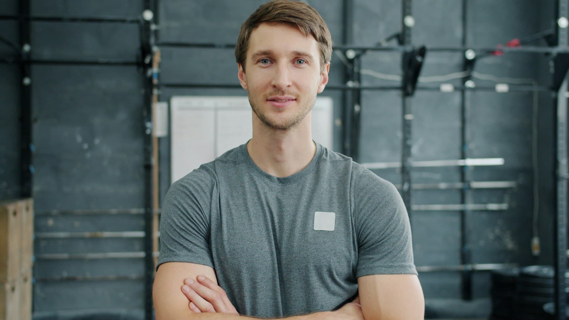 A gym owner stands on his gym floor, arms crossed