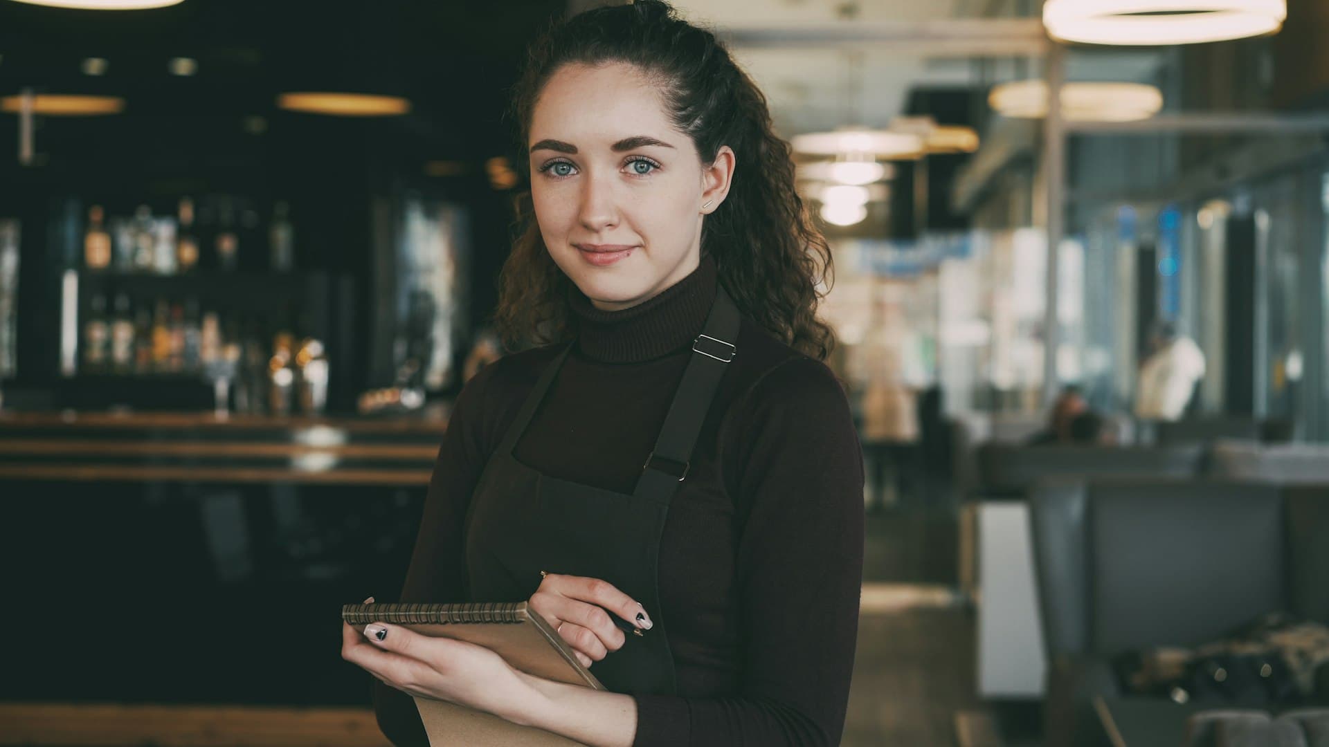 A restaurant manager in an apron, notebook in hand, in her dining room