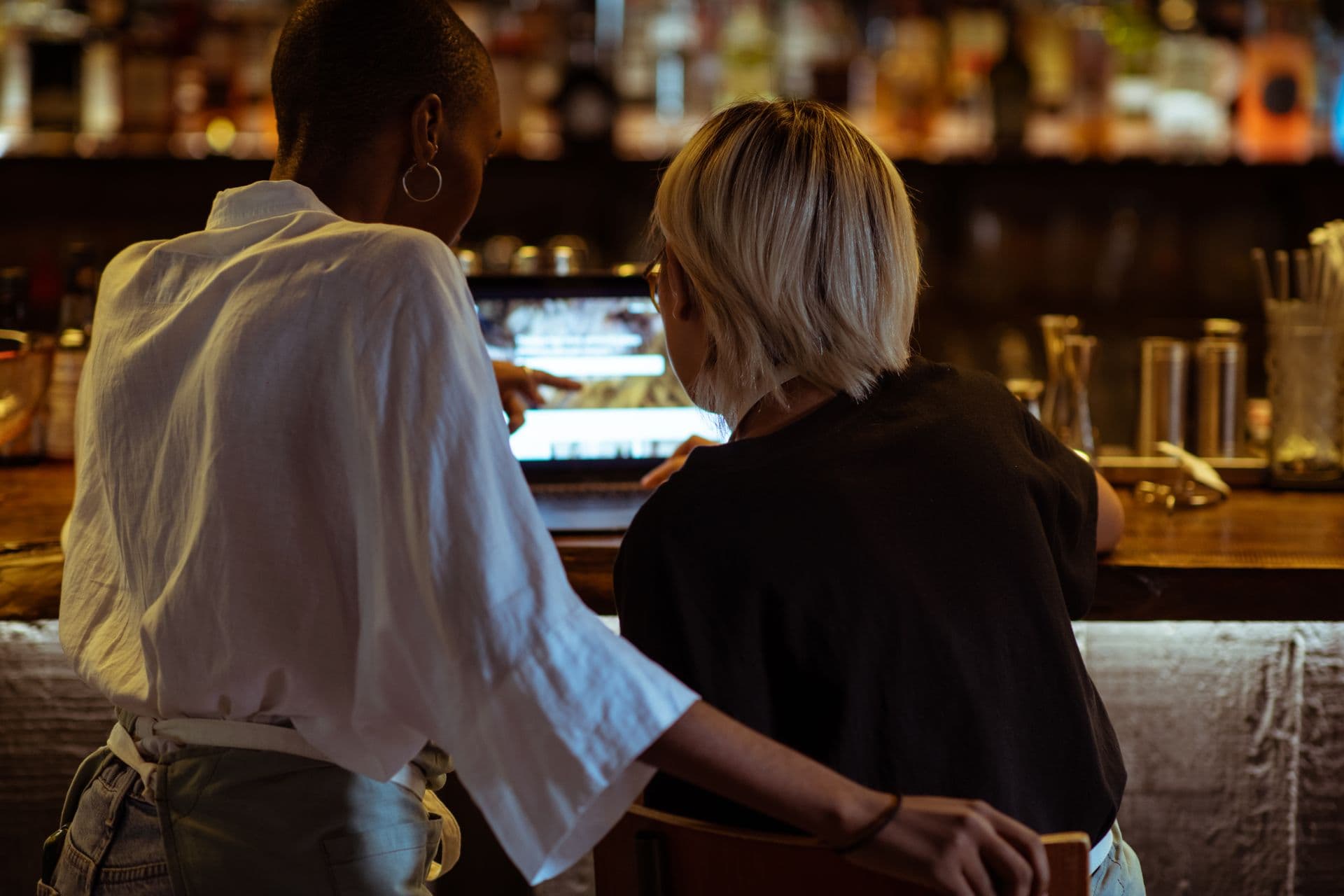 Two staff check a laptop at the bar before service